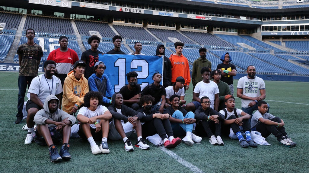 A group of students and mentors hold a Seahawks 12 flag on Lumen Field