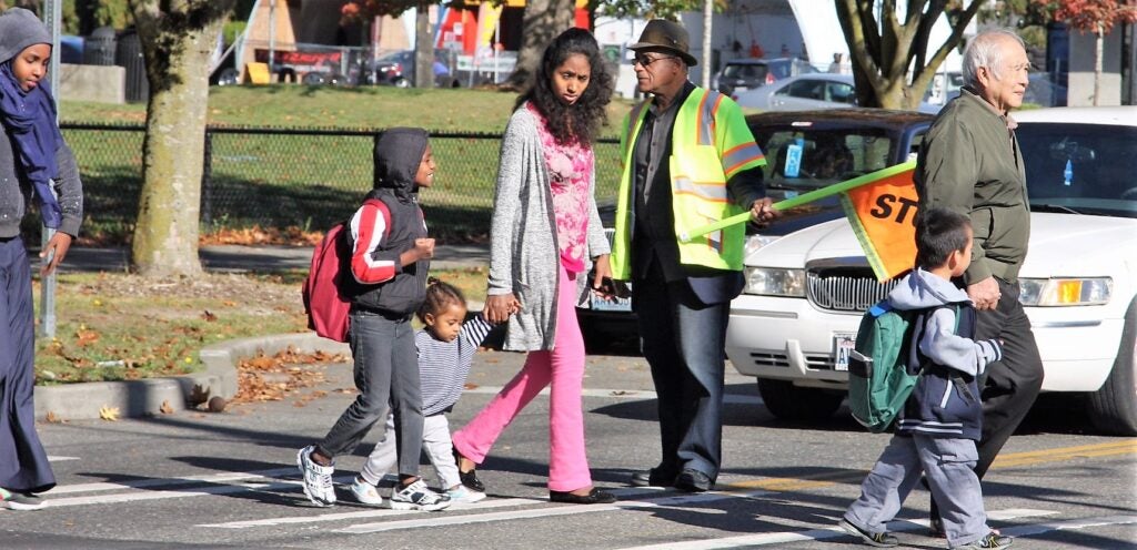 Crossing guard holds out flag as families cross the street.