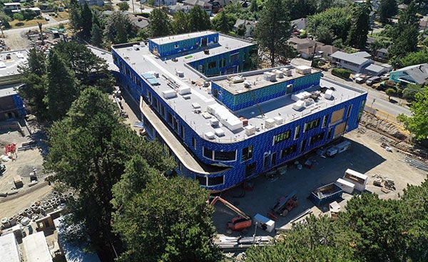 aerial view of a building under construction with a flat gray roof with skylights andblue material on exterior walls