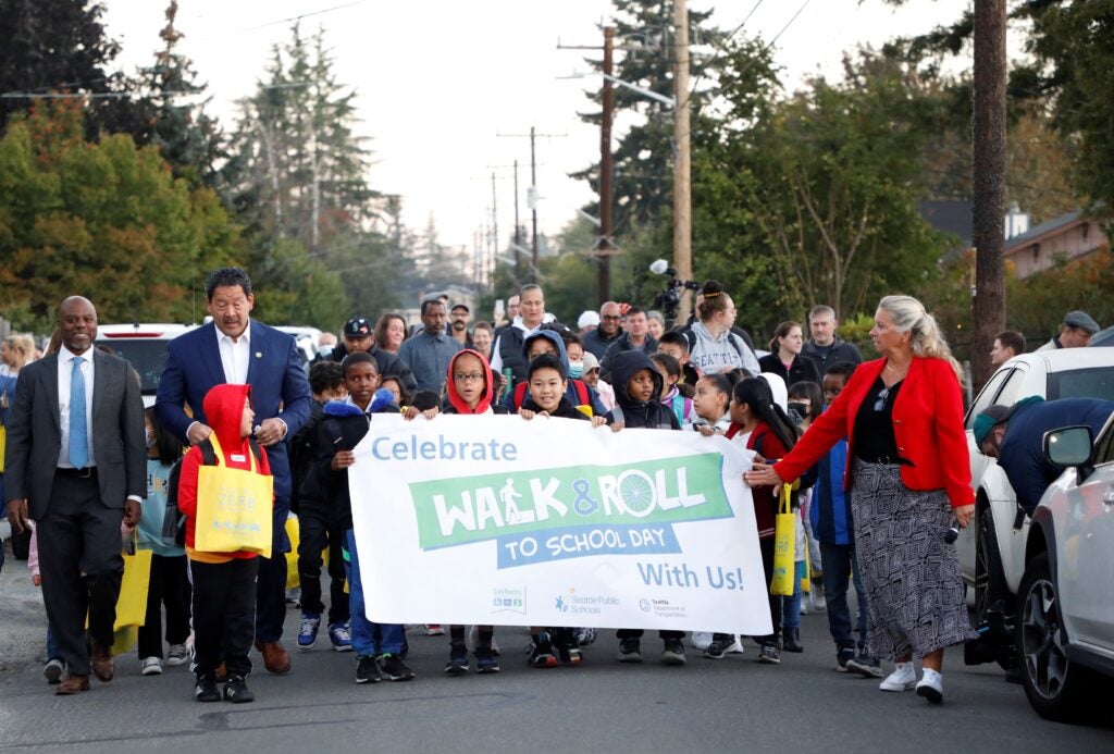 Superintendent Jones, Mayor Harrell, and Lori Dunn walk with Dunlap and South Shore students holding a sign that says "Walk & Roll to School Day"