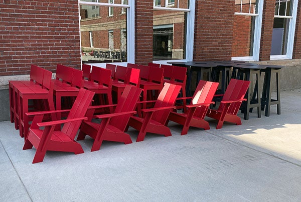 red chairs and stools, and black tall tables sit by a brick building with windows