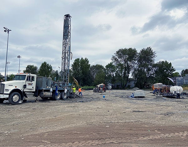 a truck with a tall drill attached and people working