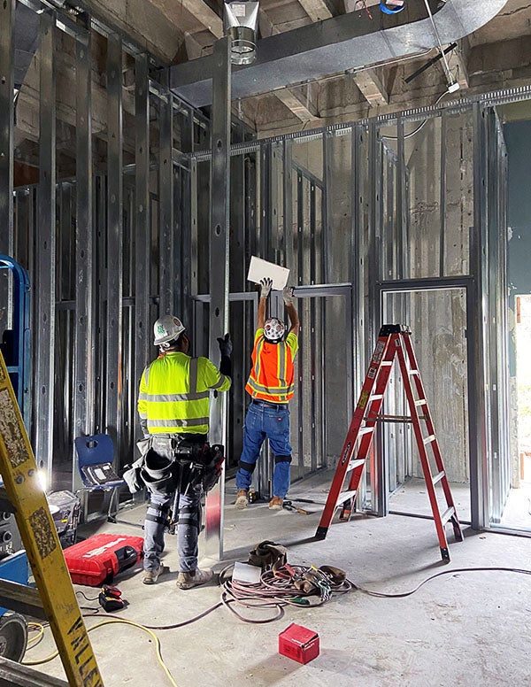two workers and a ladder in a room with metal studs for walls