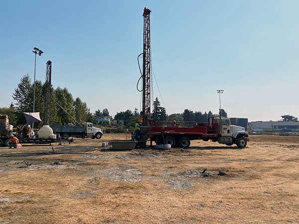 a drilling rig stands above a field of dirt covered in straw. trucks are in the photo