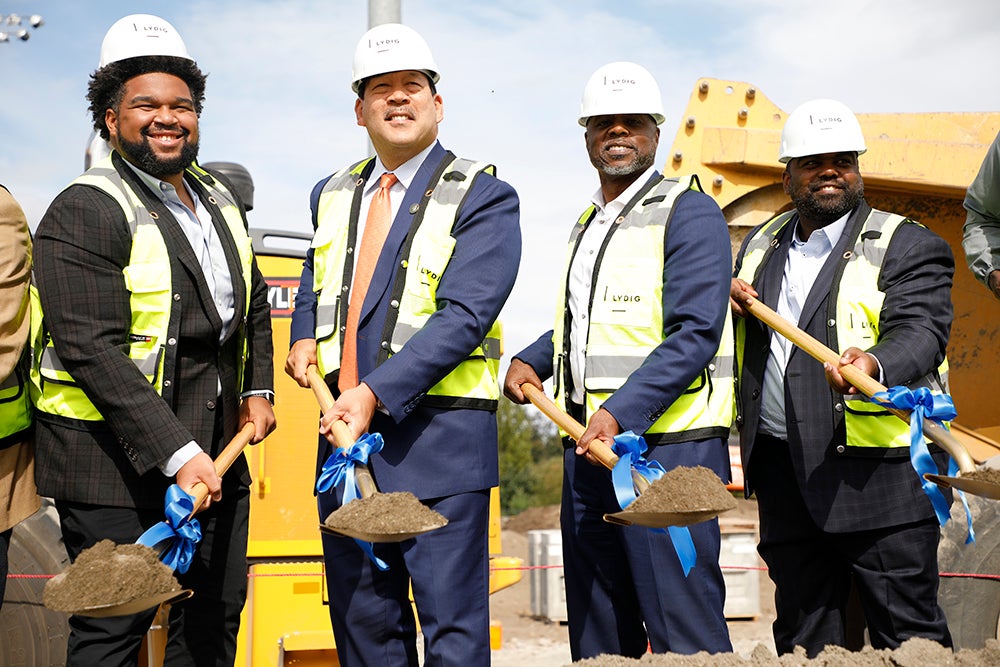 four men in suits lifting shovelsful of dirt