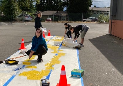 Four women paint on a sidewalk on a playground