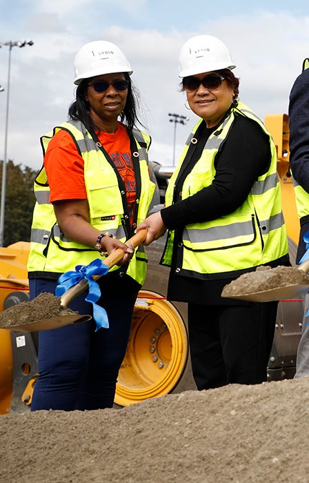 two people holding one shovel with dirt in the scoop portion
