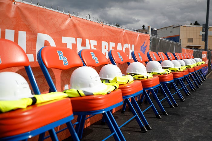 a line of orange chairs hold construction hats and yellow vests