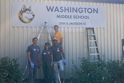Four volunteers stand near a school sign