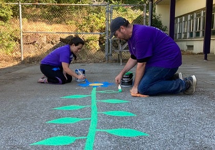 Two people paint a plant on a school playgroup sidewalk