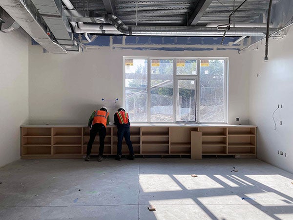two workers installing low shelving under a window