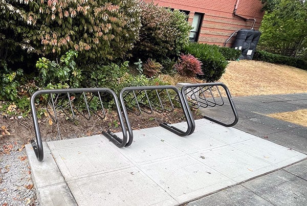 a bike rack in front of plants with a brick building