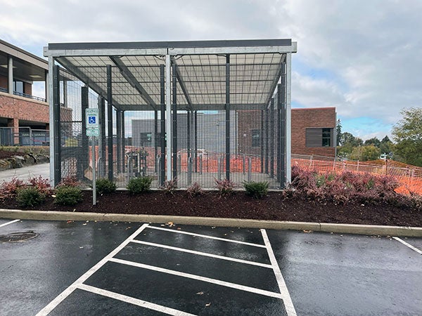 a fenced in space with bike racks inside and plants on outside