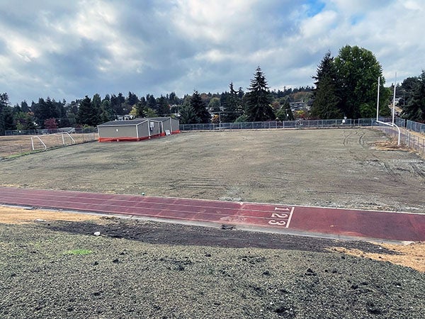 a field and track has portables in one corner and green-gray material on dirt