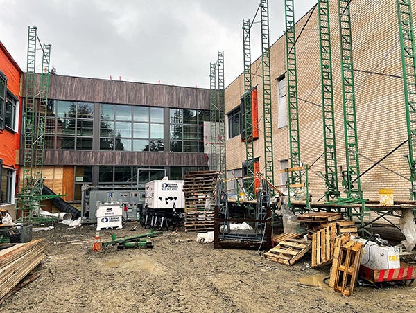 a building under construction with brown siding and windows on one side and bricks on another with metal scaffolding on both