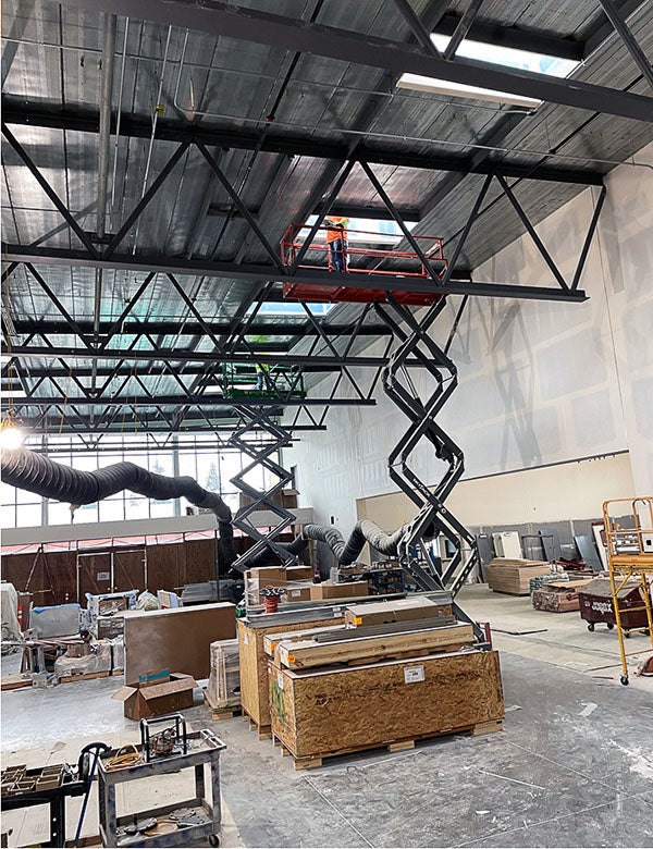 a scissor jack has a person working near the ceiling of a large room under construction