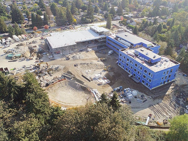 aerial view of a large L shaped building under construction with large holes dug in ground