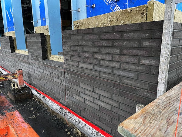 a masonry wall going onto a building with varying colors of bricks