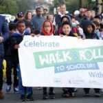 Students holding sign for walk and roll to school day with Superintendent Jones and Mayor Harrell