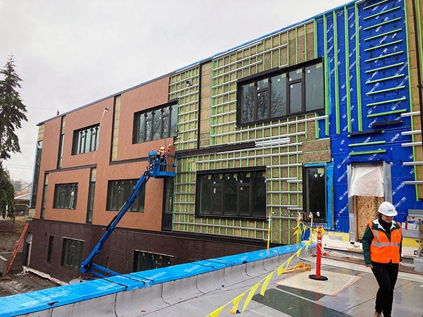 a three story buildng with workers installing brick masonry from a lift