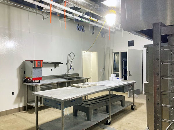 a large room with a ceiling grid, a counter with sink/faucet and a metal work table