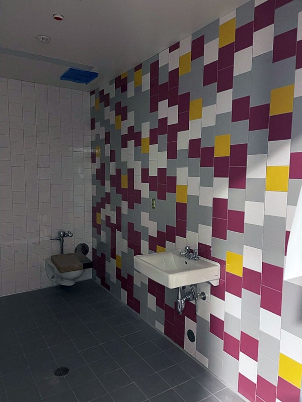 a purple, yellow, white, and gray tiled wall with a sink and a toilet