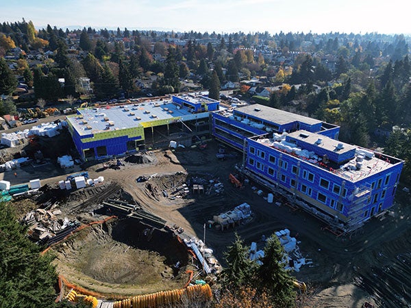 aerial photo of an L shaped building with a dirt area in front that includes a large hole