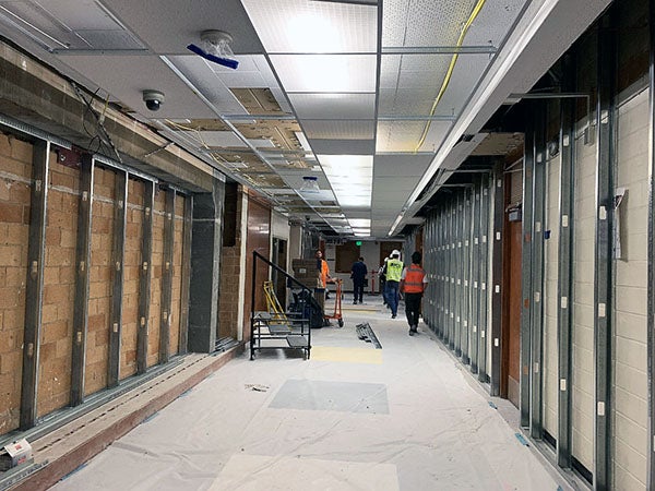 a hallway has metal walls supports over masonry blocks with construction workers walking down hall