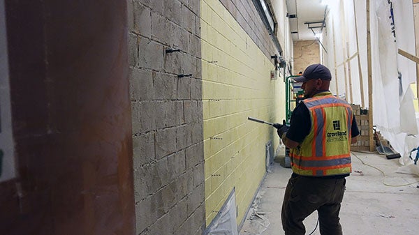 a worker has a large drill in front of a masonry wall in a space under construction