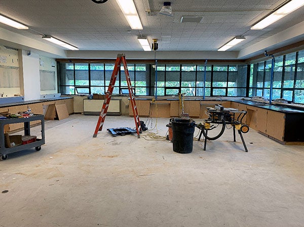 a large room with windows has cabinets partially installed, a ladder, and a table saw