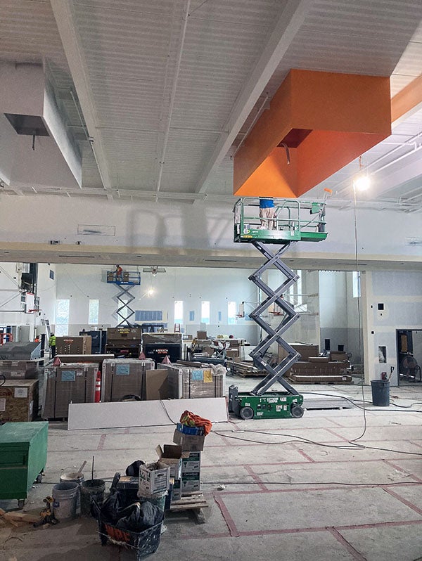 a large open indoor space has scissor lifts with workers painting areas of ceiling fixtures