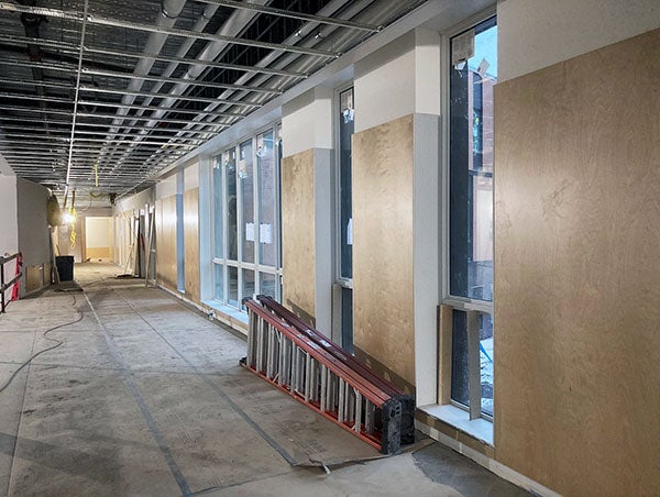 an unfinished interior corridor has windows interspersed with wood wall panels and a celing grid