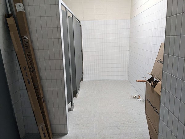 white tile walls with three toilet stalls on the left