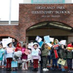 A group of students gathers in front of their school with signs