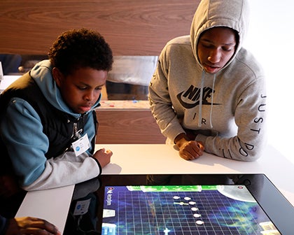 Two students watch as an other student plays a game
