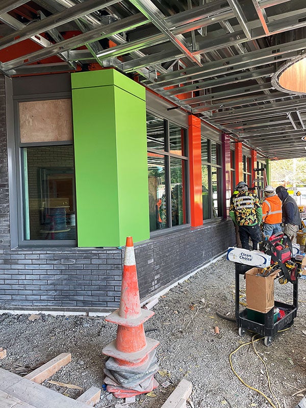 a corner of a building has ceiling girders showing brick goes part way up the wall. a green corner is between windows