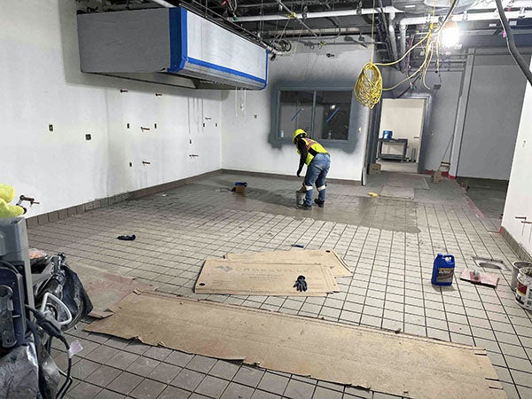 a person is puting liquid on one section of a concrete floor with tiles that have no grout in the foreground