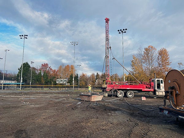 a tall drill machine with a person in a hard hat stands in a muddy field