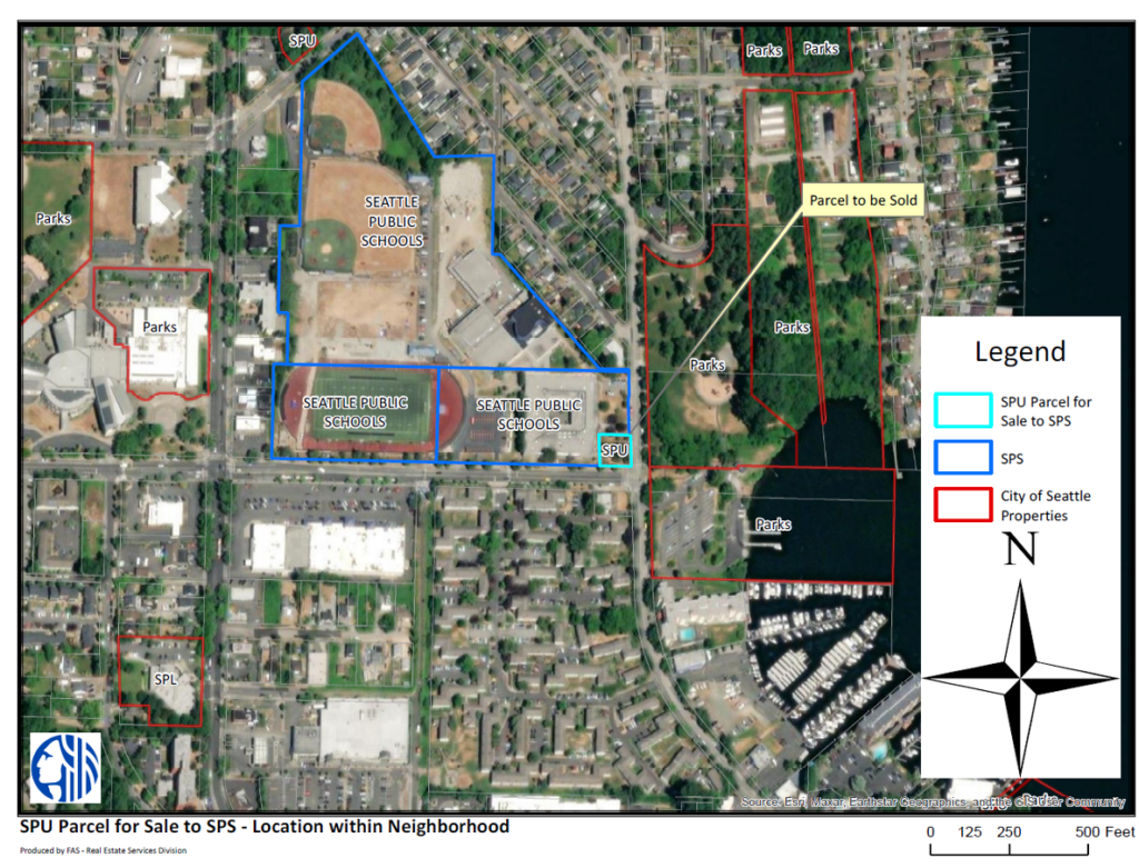 aerial view of several blocks of a neighorhood. In the center, a blue outline defines three parcels, each marked Seattle Public Schools. Within the lines you can see a track and field, other playfields, a large square building with a courtyard, and some other large buildings. In the lower right of the blue outline, there is a lighter blue square labled Parcel to be sold. Other parcels on the map are outlined in red and marked Parks. There are other buildings and homes throughout the area. A body of water is on the right side. A legend denotes SPU parcel for sale, SPS, and City of Seattle Properties