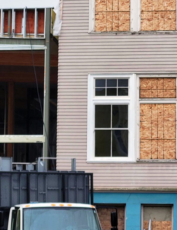 an exterior wall with one window showing and the other windows boarded up