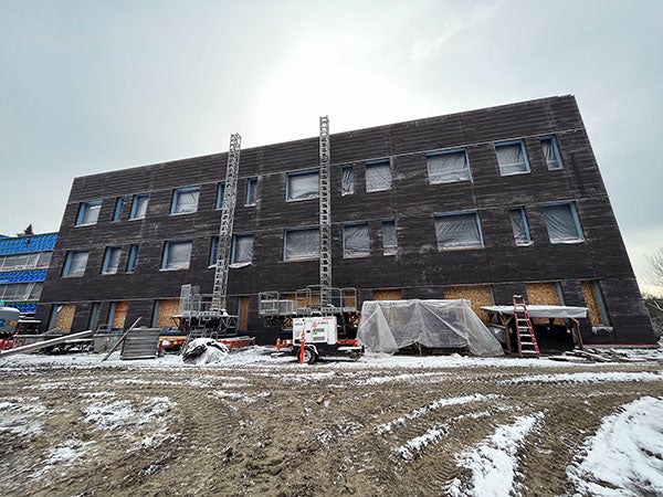 a three story brick building has boarded up window spaces on first floor and plastic covered window holes on levels 2 and 3. construction equipment is in the foreground