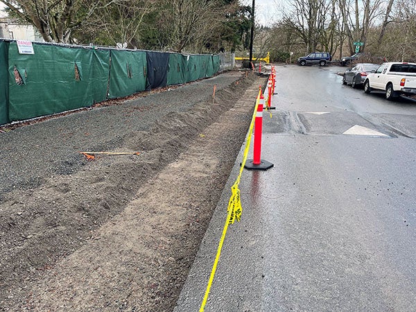 a street with a dirt and gravel area next to it and a fence behind that