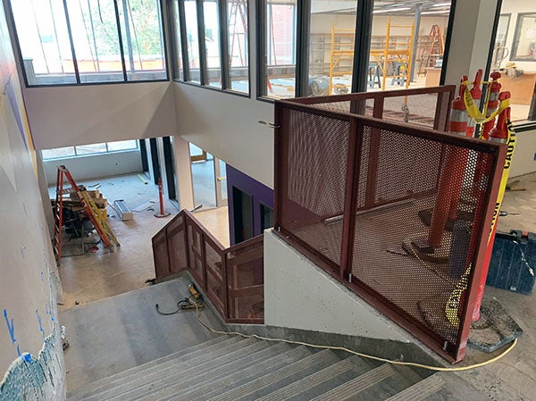 looking down concrete stairs with a metal grid railing on the landing next to the stairs