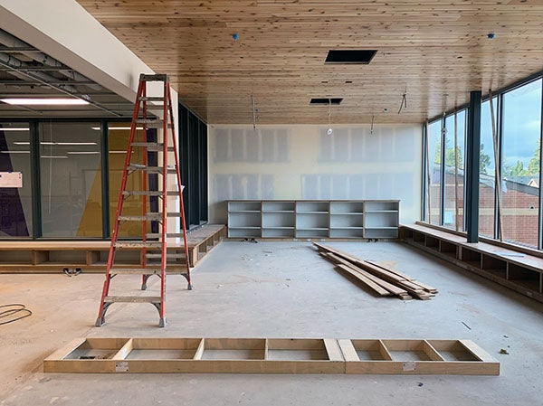 a large room with windows to the outside on one wall and windows to the inside on another. the ceiling is wood and there are some shelves against the wall. a ladder is in the middle of the room