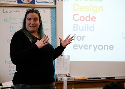 A teacher stands in front of a white board talking with students