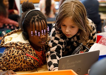 Two students work together on a laptop in a classroom