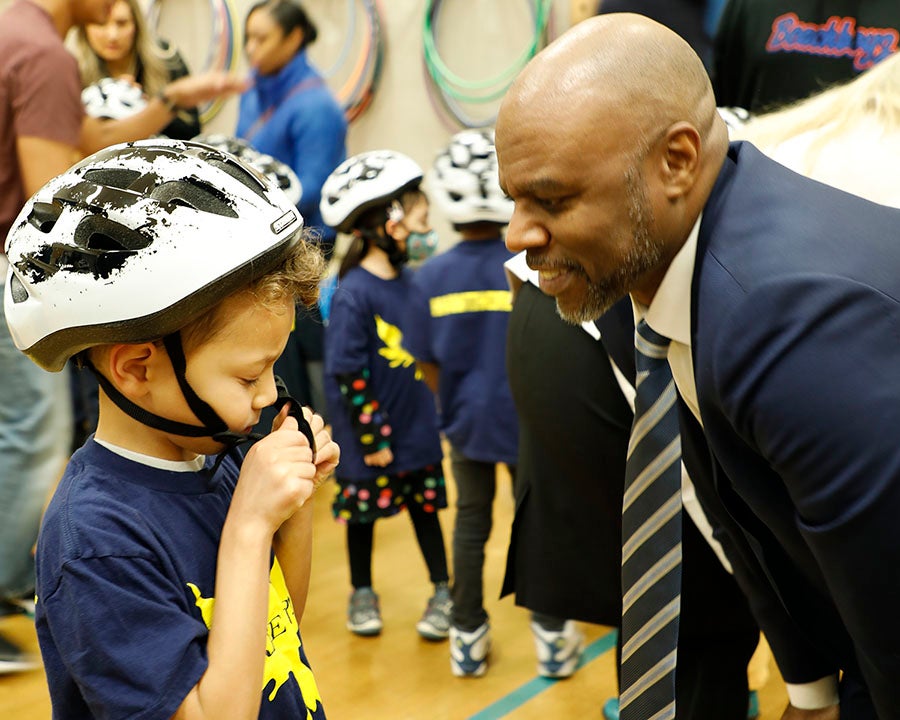 Superintendent Jones smiles at a student while they put on a bike helmet 