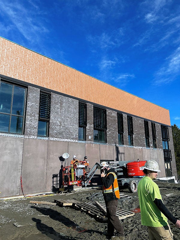 exterior of a building under construction with half height concrete wall with bricks around windows and metal panels on top