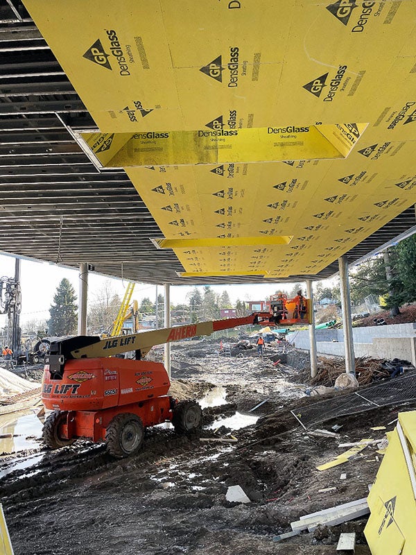 a muddy outdoor area has a partially completed roof with yellow material being installed