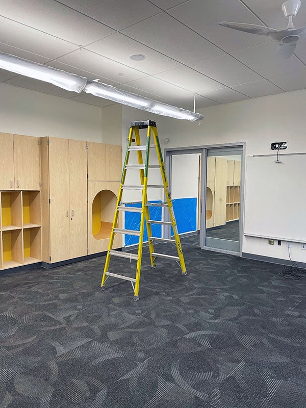 a large room has cabinets, carpet, and a ladder
